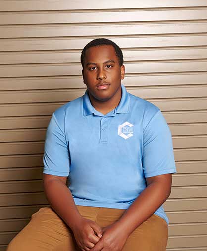 Andre Johnson Headshot A young man in a light blue polo and khaki pants sits calmly against a tan backdrop.