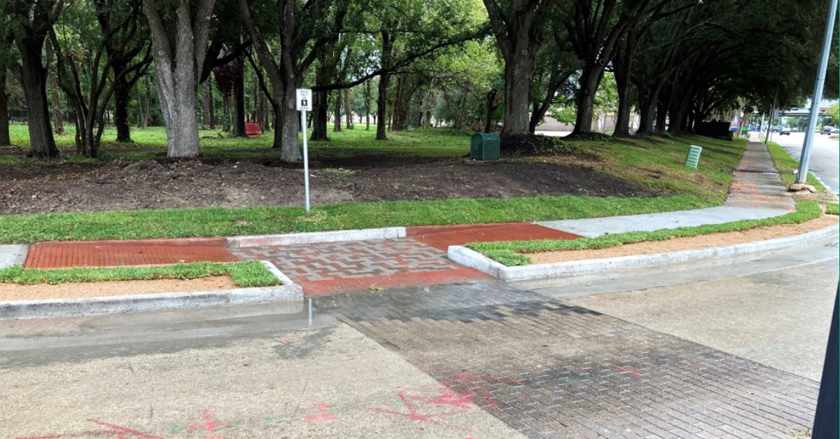 A completed curb and sidewalk improvement shows a brick-patterned pedestrian crossing with new curbs and accessible ramps along a tree-lined roadway after construction.