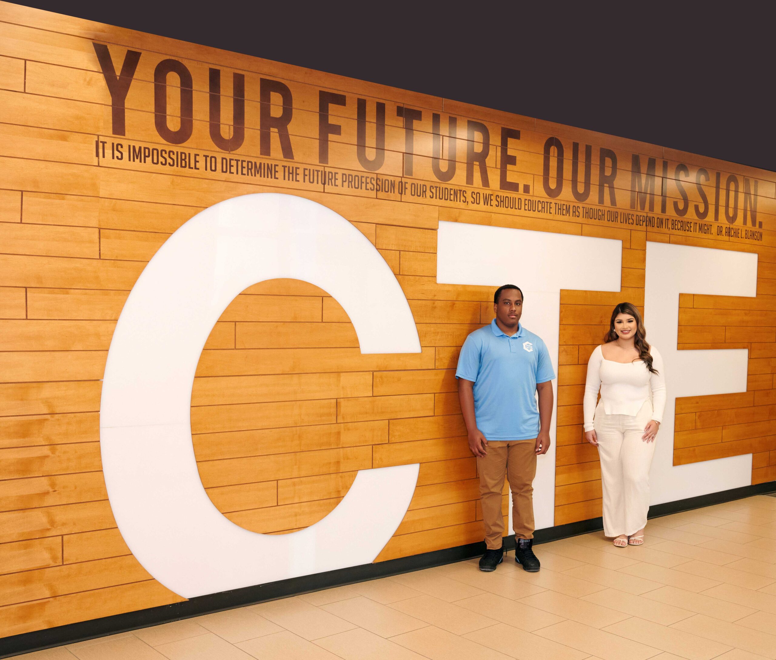 CTE Wall Students Two students stand side by side in front of a large wood-paneled wall that says CTE – Your Future. Our Mission.