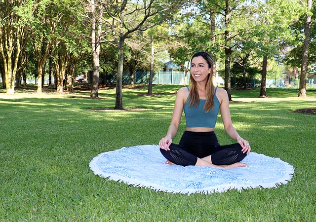 A woman sits cross-legged on a blanket practicing yoga on a grassy lawn at City View Park, surrounded by trees and open green space.