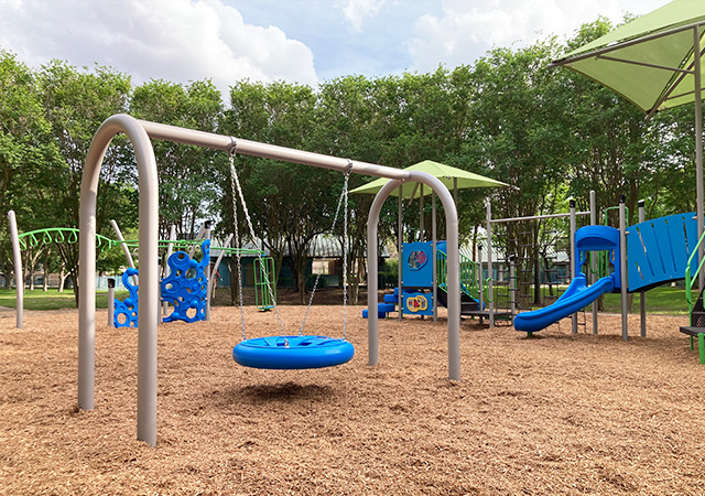 Large playground area at City View Park with slides, climbing features, and shaded play structures designed for children. Trees and mulch surfacing surround the playground.
