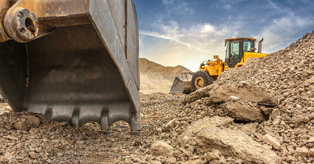 North Belt Substation Newsroom Graphic Close-up of a large excavator bucket in the foreground and a yellow front loader in the background, surrounded by mounds of dirt at an active construction site under a partly cloudy sky.