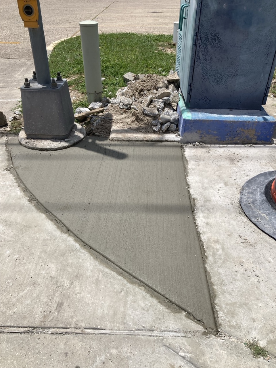 A triangular section of freshly laid concrete near a signal pole and utility box, enhancing walkability and safety at the intersection.