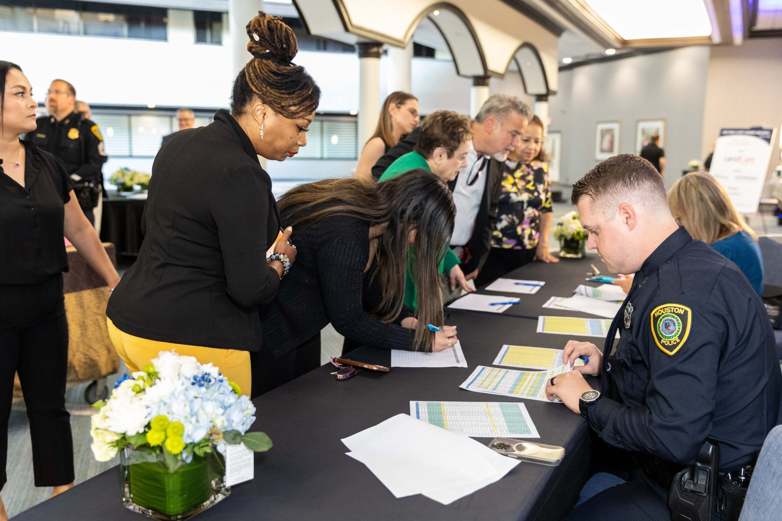 Guests sign in at the registration table as an HPD officer assists; sponsor signage and floral decor are visible.