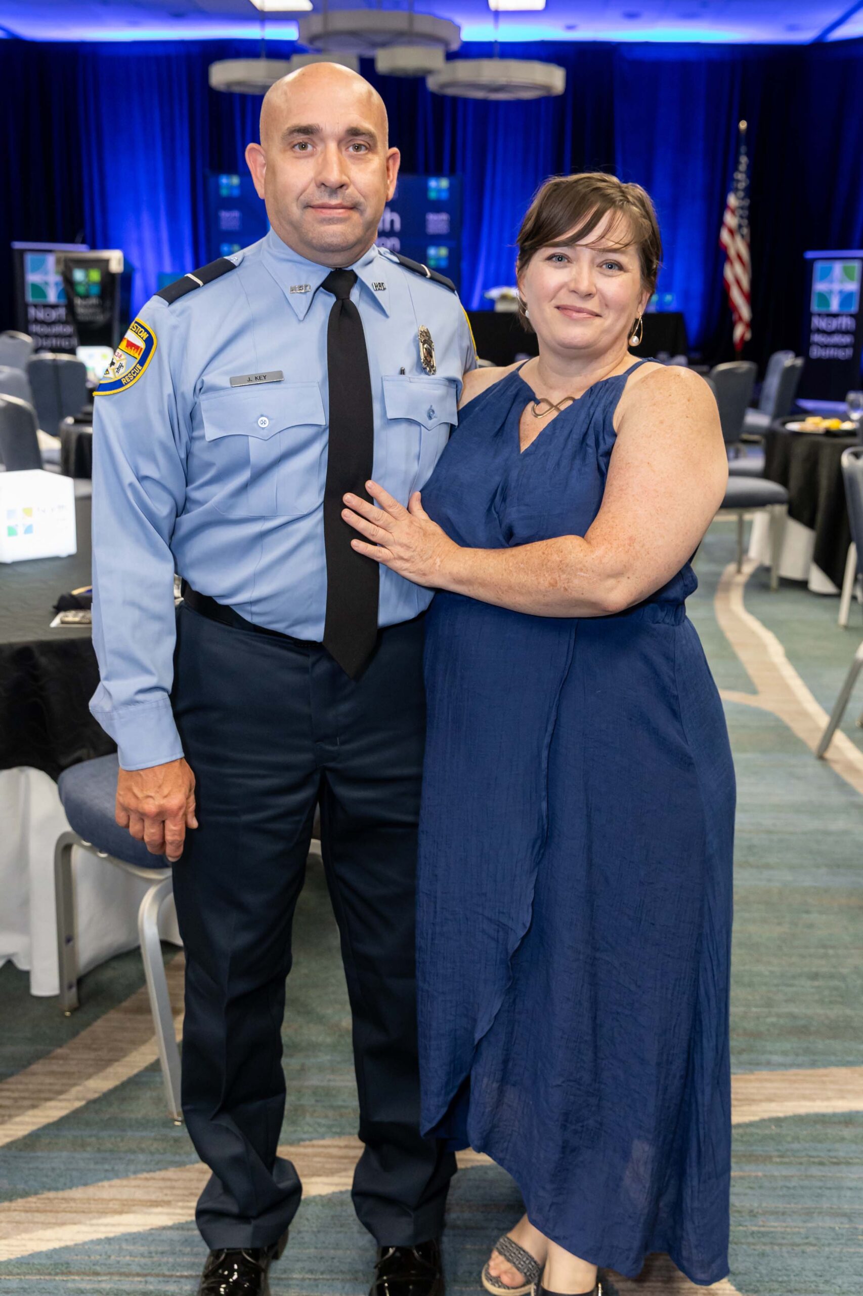 A uniformed HFD officer stands beside a woman in a navy dress, smiling inside the decorated event room.