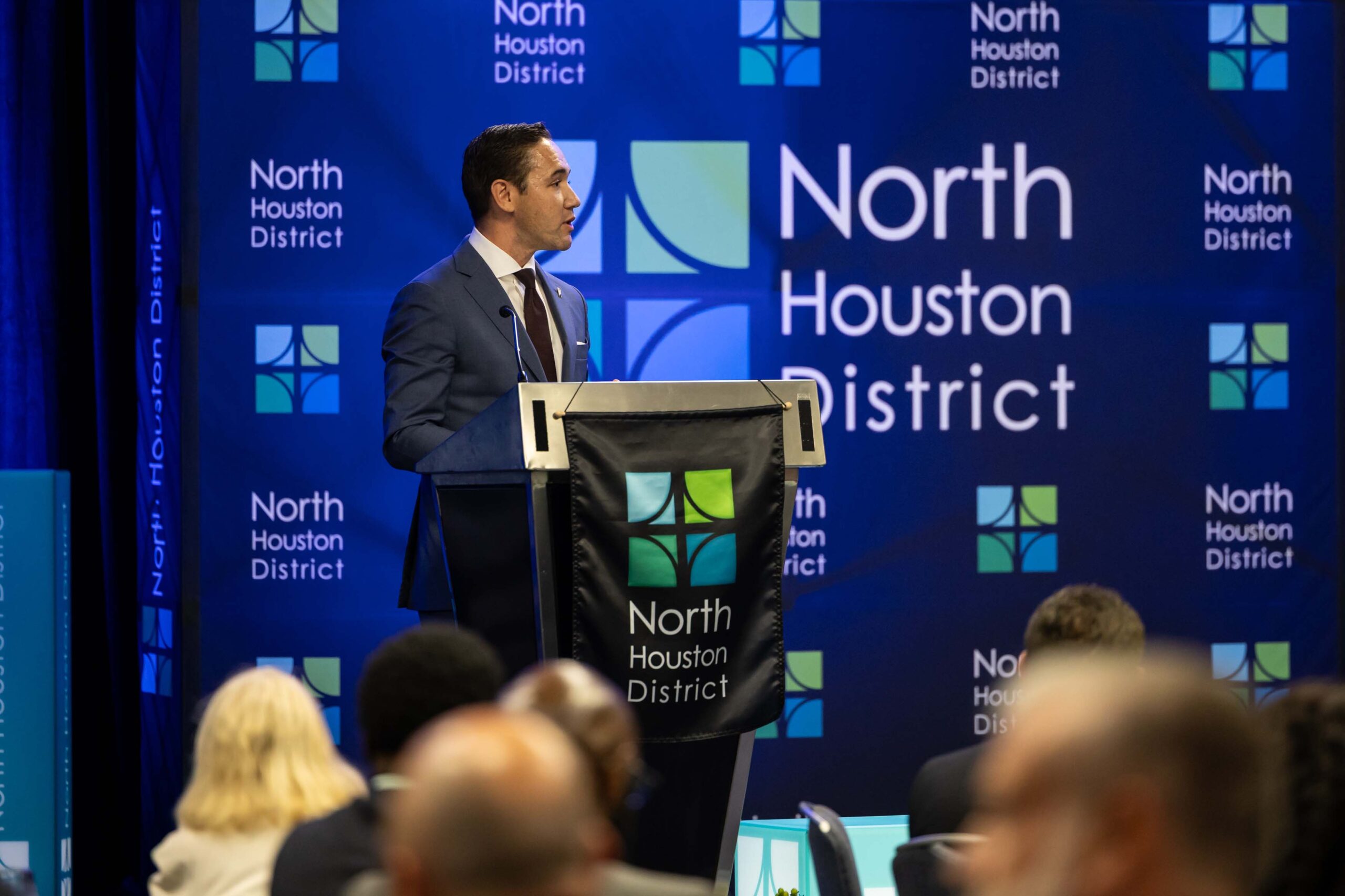 A speaker at a podium delivers remarks during the 2025 Public Safety Awards Luncheon, with a North Houston District backdrop.
