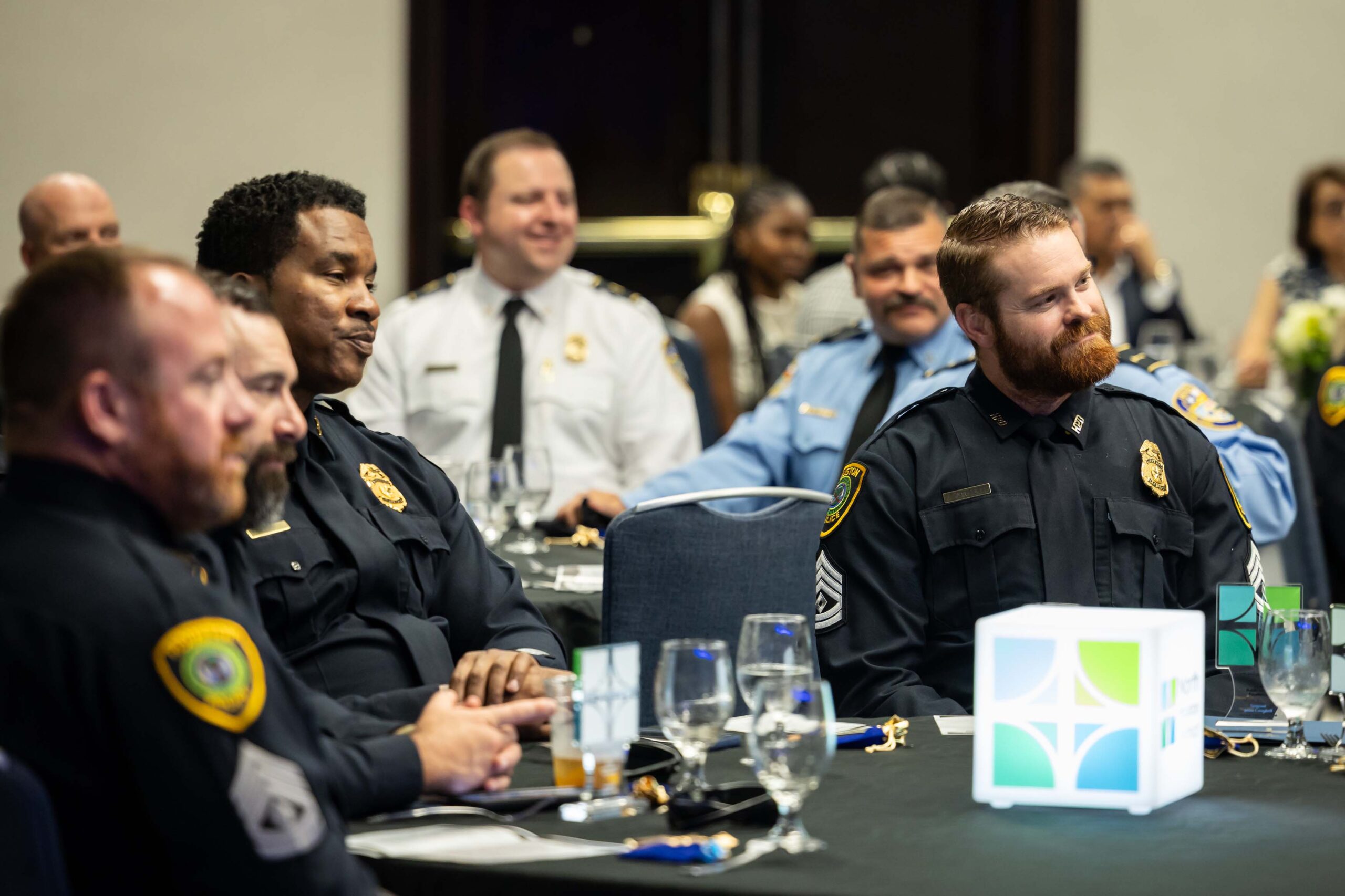 Law enforcement officers and public safety leaders seated at a banquet table, smiling and listening during the awards program.