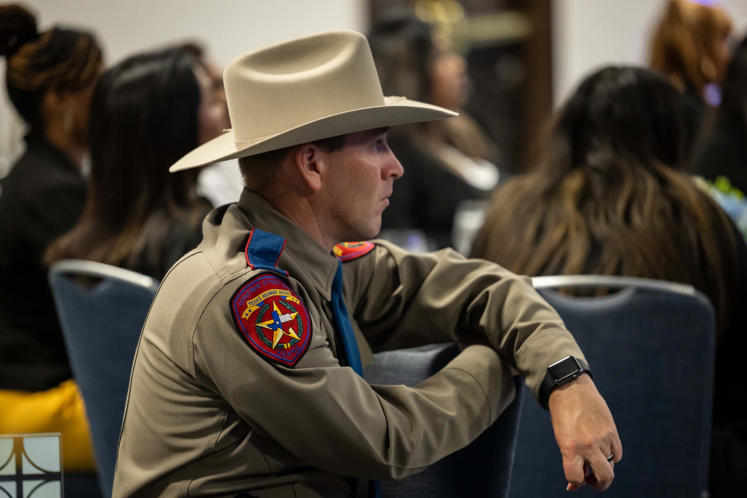 A uniformed Texas Highway Patrol officer with a cowboy hat sits at a round banquet table, facing the stage.