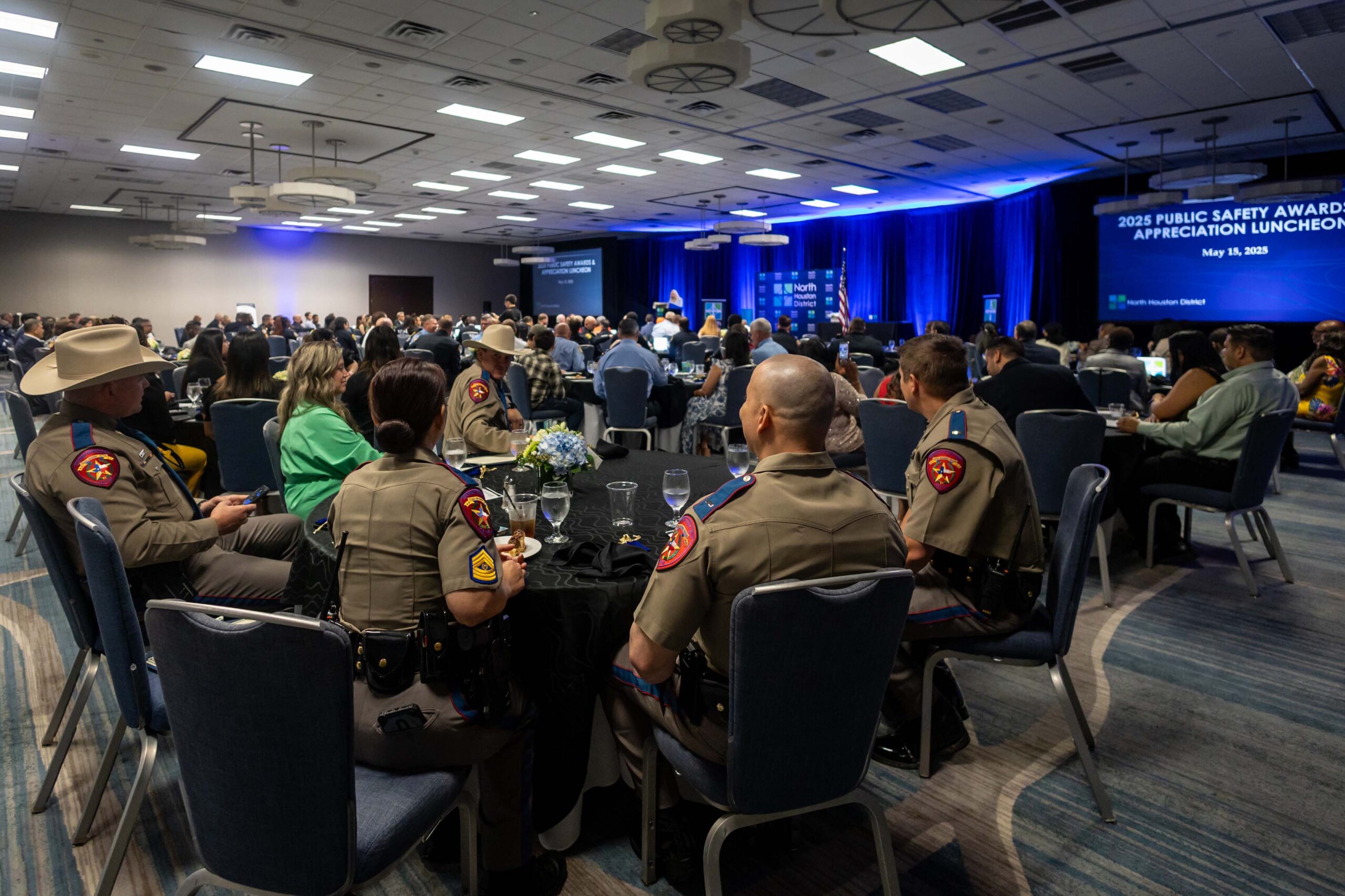 Uniformed officers and guests are seated around a banquet table watching the stage during the program.