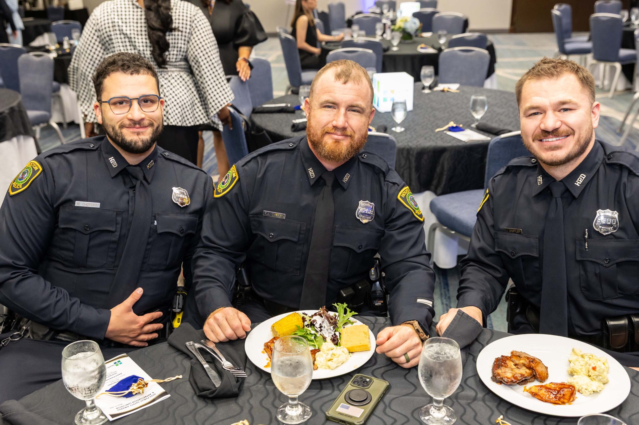 Three uniformed officers sit at a round table, enjoying their plated meals.