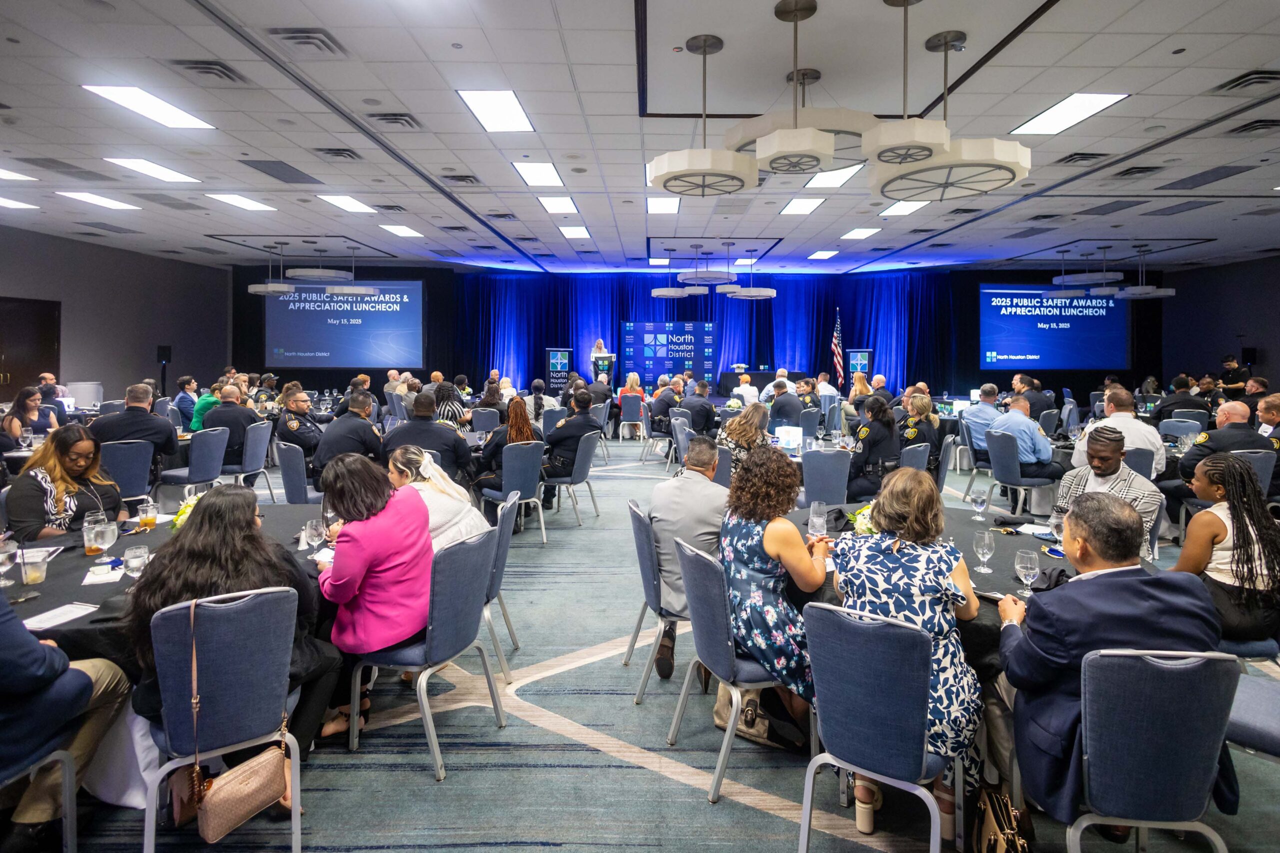 A full-room shot of the event shows attendees at round tables watching the awards program on stage.