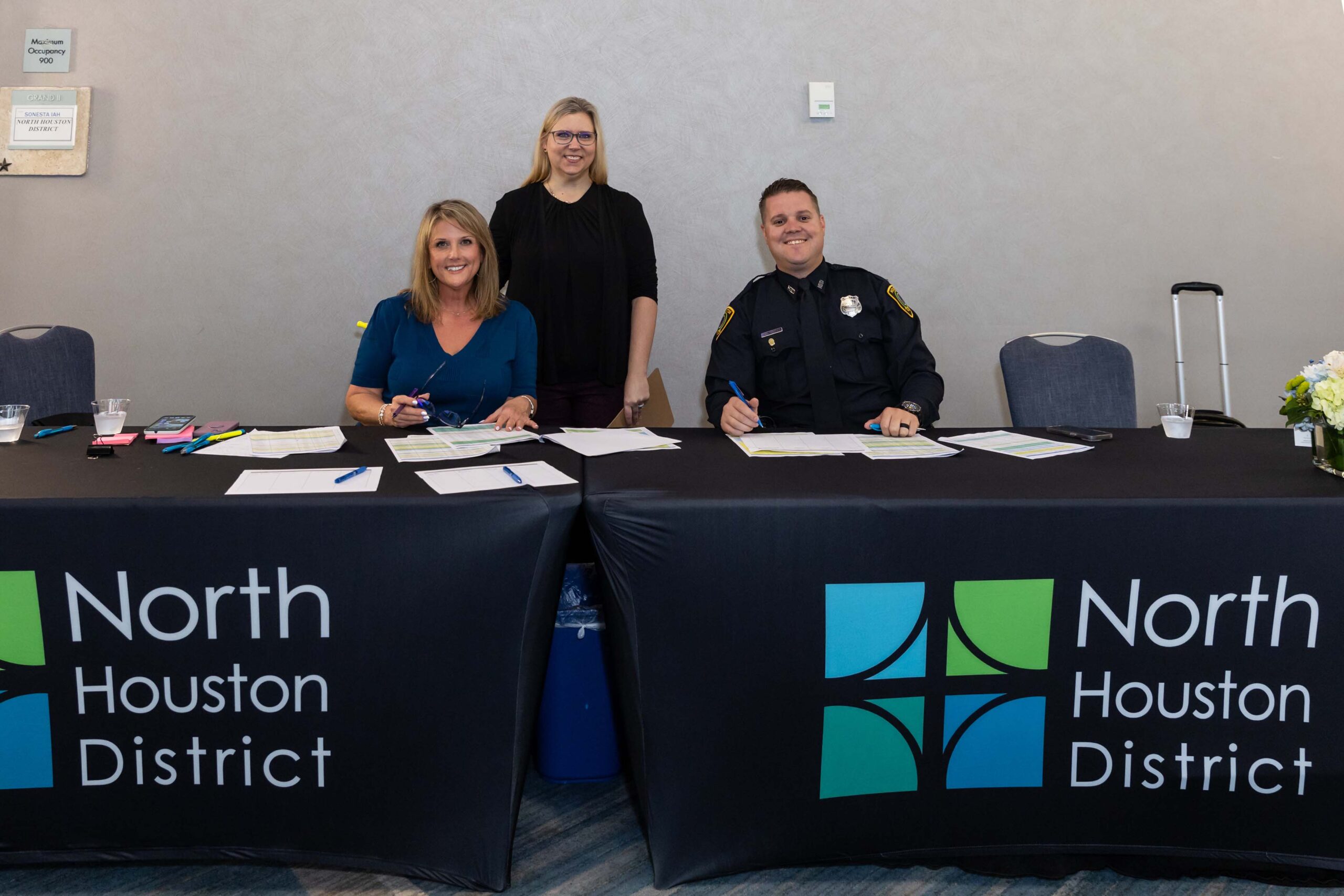 Two staff members and a uniformed officer welcome guests from a North Houston District check-in table.