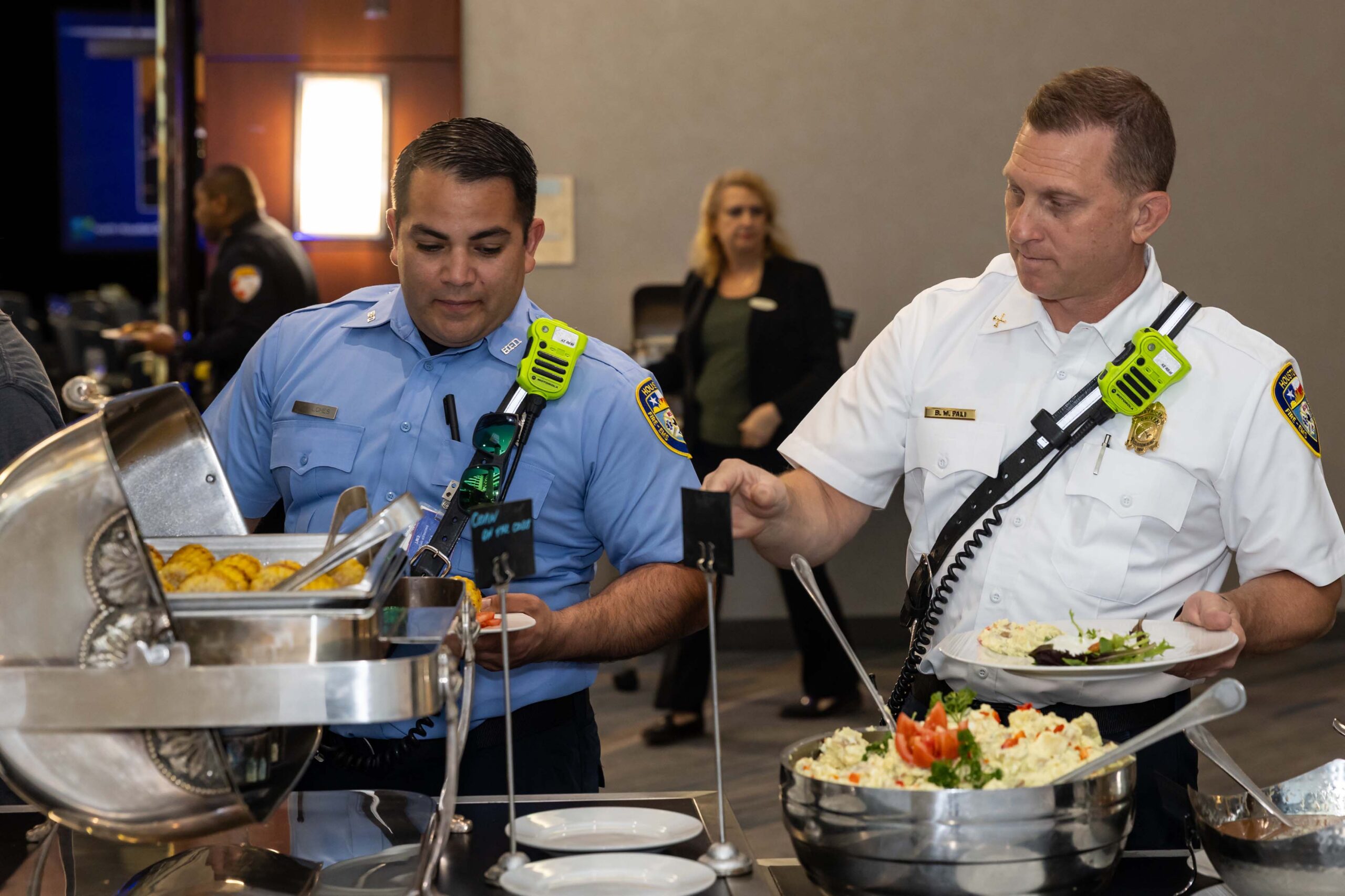 Two uniformed firefighters serve themselves from a buffet line at the luncheon.