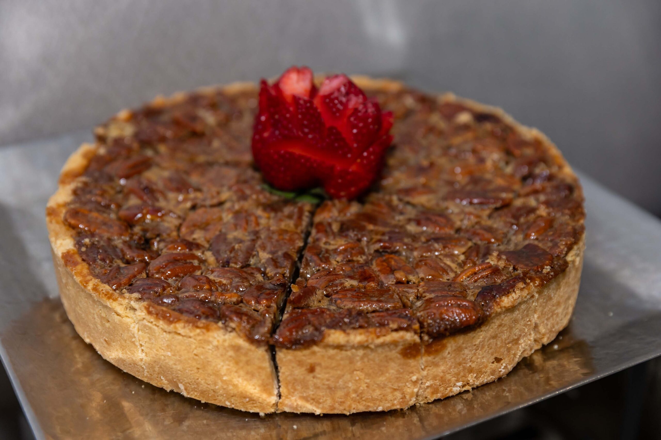 A pecan pie topped with a carved strawberry sits on a silver tray.