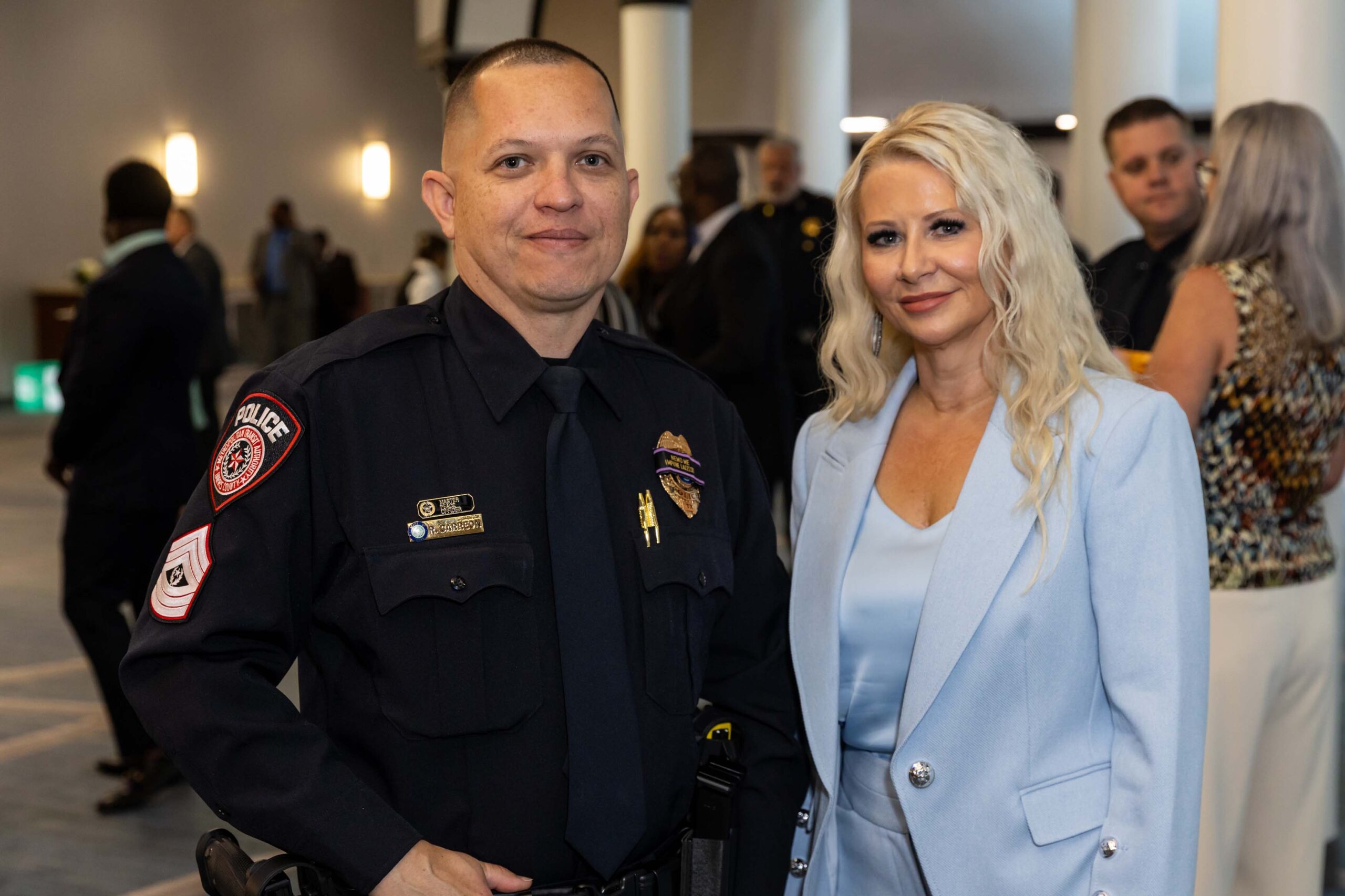 A uniformed officer and woman in a light blue suit pose for a photo in the lobby.