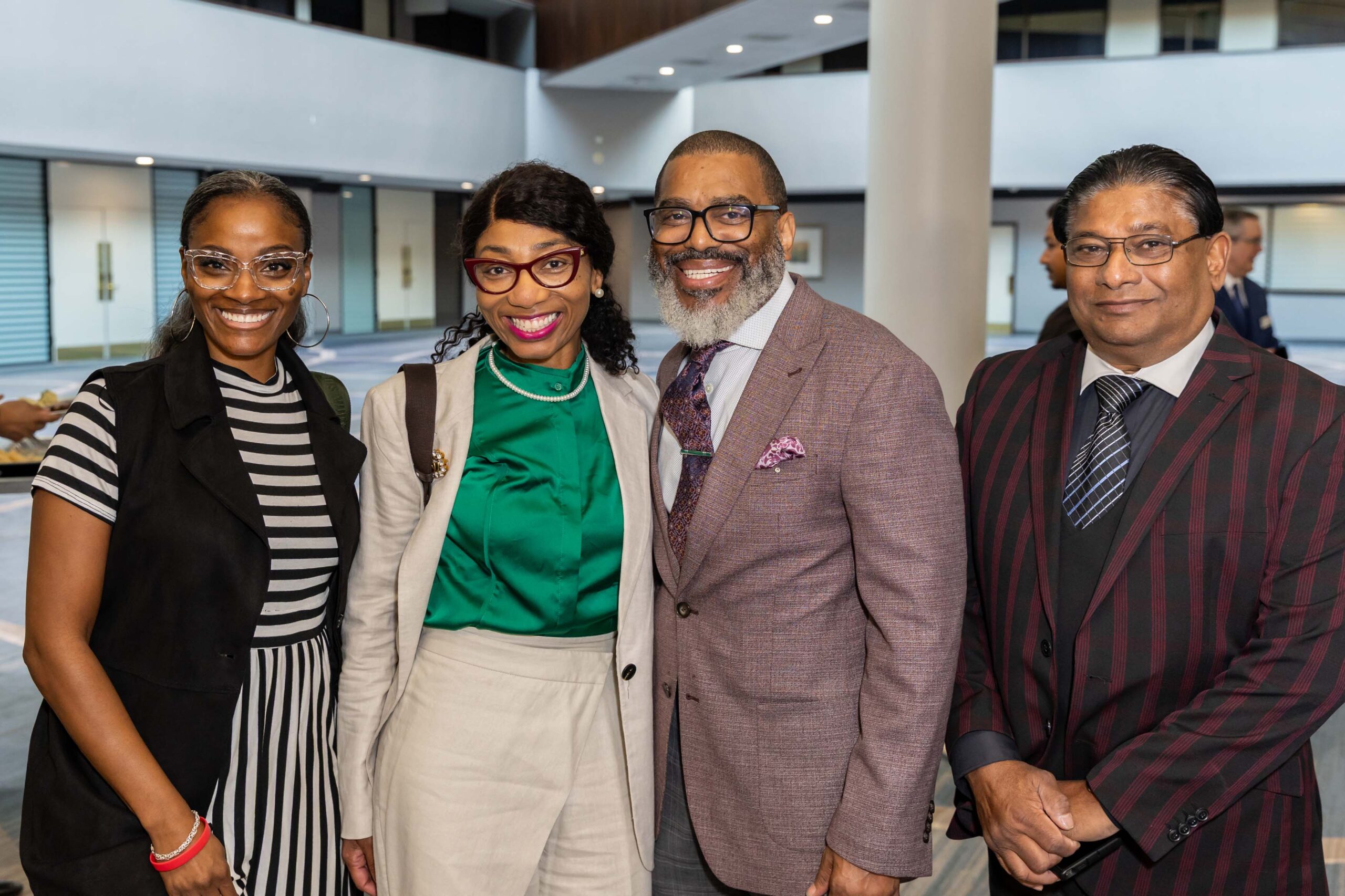 Four attendees pose and smile together in the open lobby area.