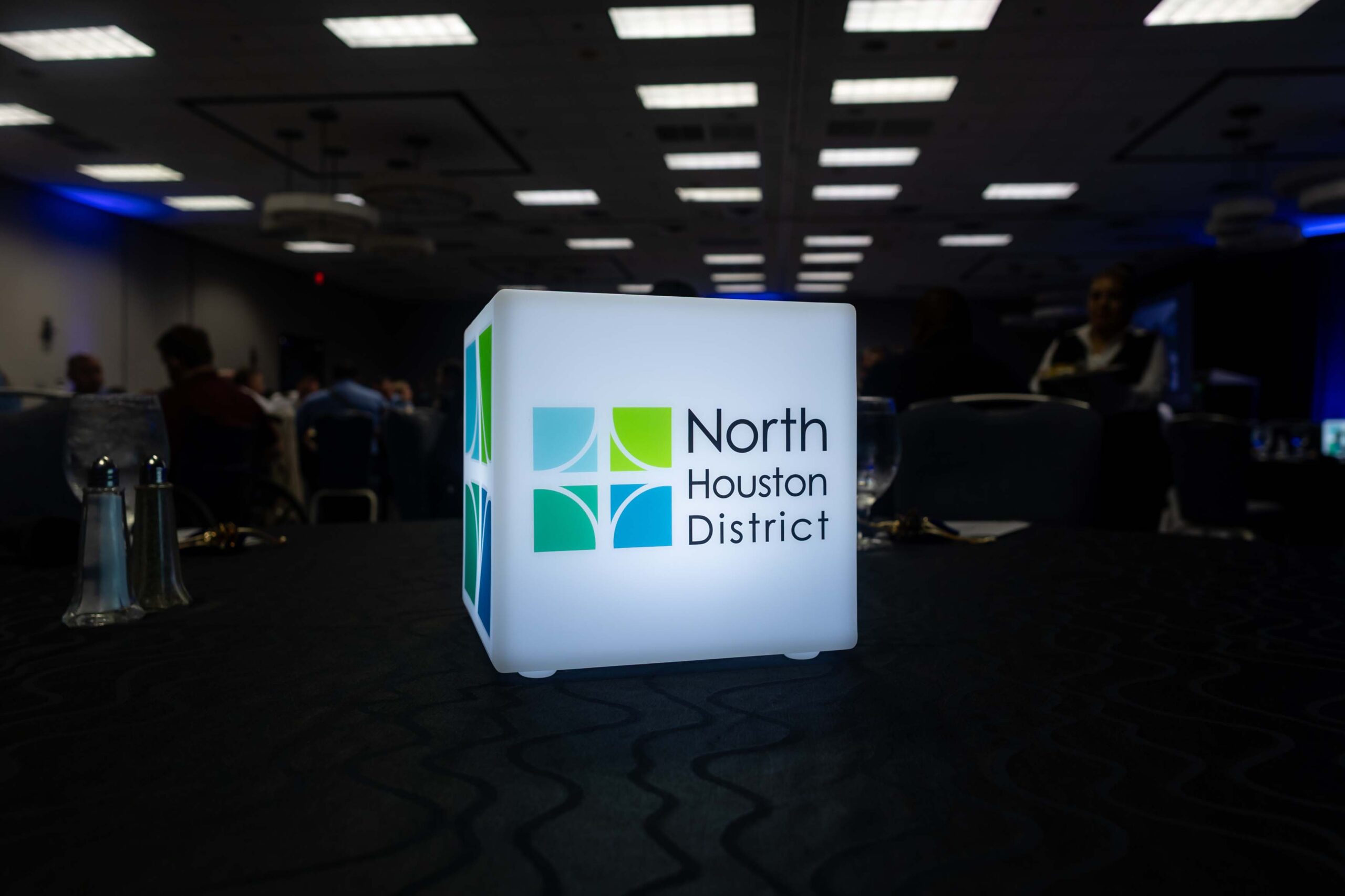 An illuminated North Houston District cube centerpiece sits on a black tablecloth.