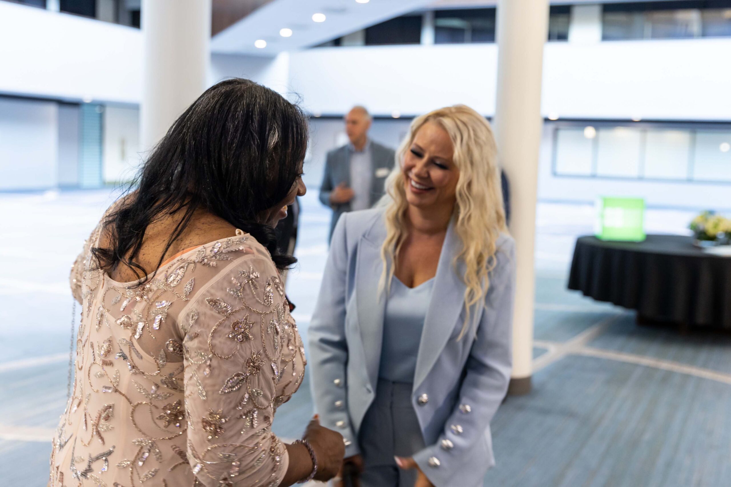 Two women smile and chat in the venue lobby.
