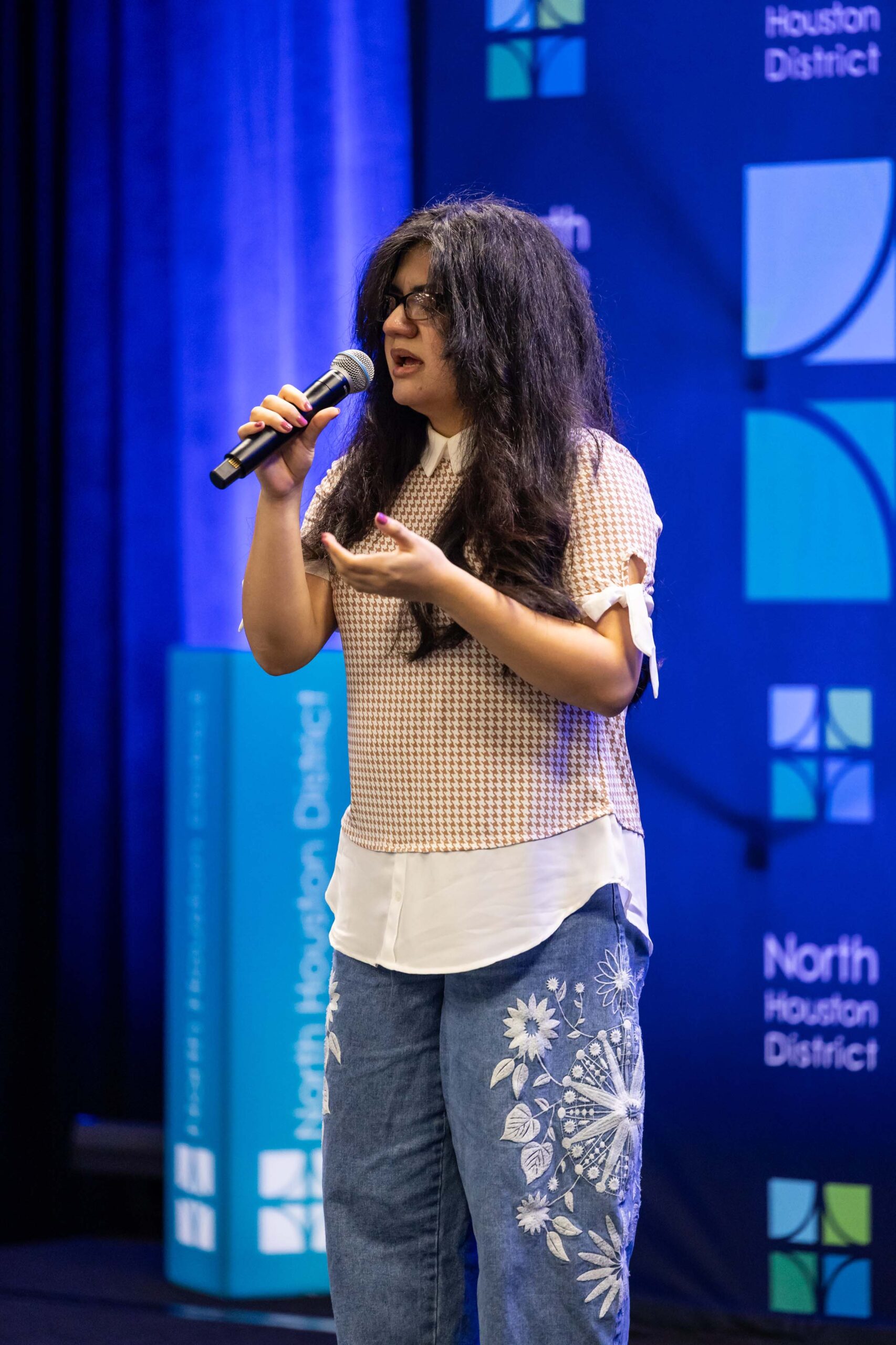 A young woman sings into a microphone on stage.