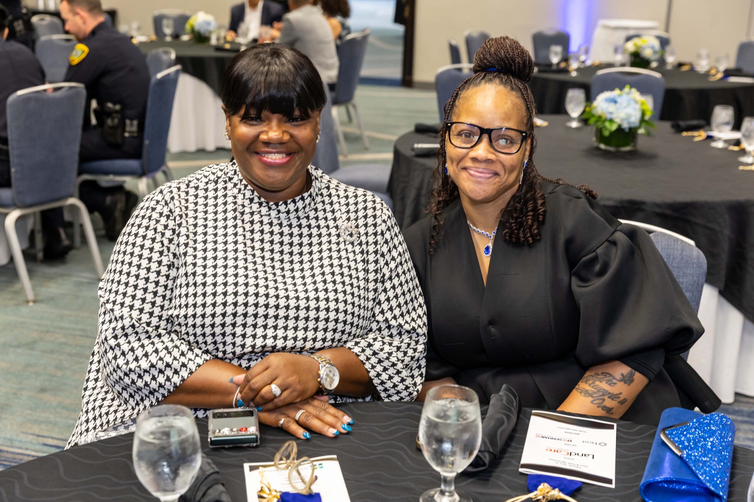 Two seated guests smile at their banquet table with programs and event materials in view.