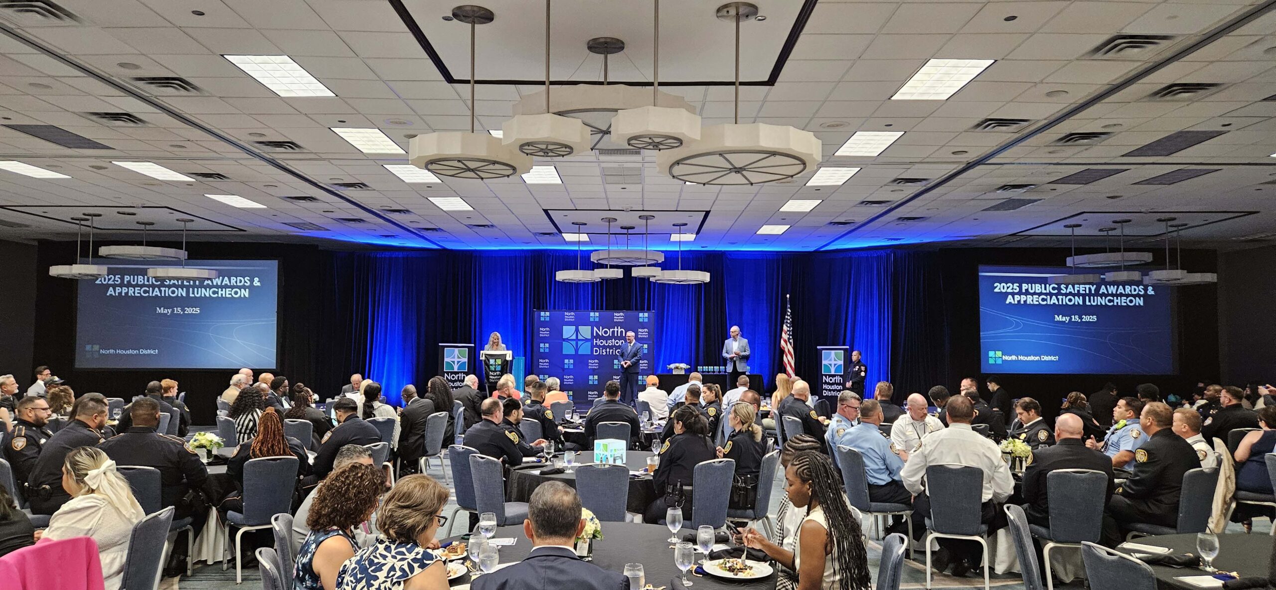 Wide ballroom view of seated guests at the 2025 Public Safety Awards Luncheon with presenters on stage and large screens behind them.