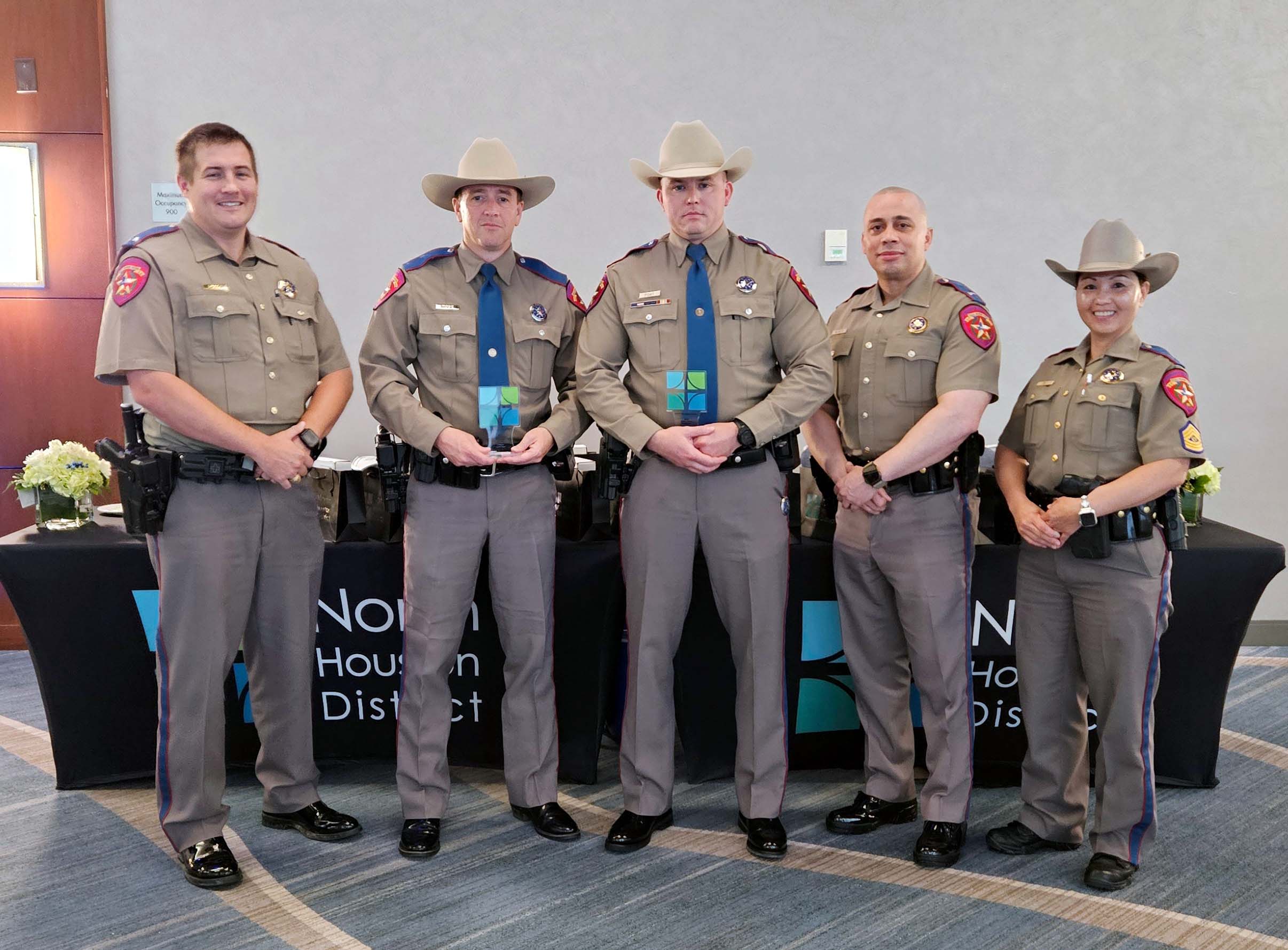 Five Texas DPS troopers pose indoors; two officers in the center hold award plaques in front of a branded table.