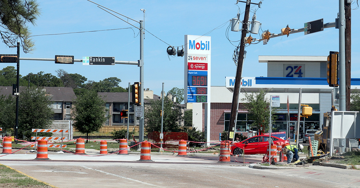 Roadway construction underway at the intersection of Rankin Road and Ella Boulevard in the North Houston District. Traffic barrels, construction crews, and utility work are visible near a gas station and surrounding businesses.
