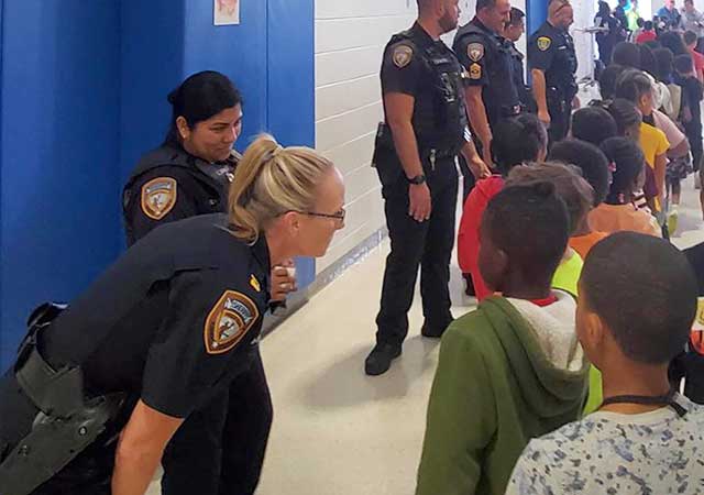 Captain Sandra Chapa and other officers interact with children at a school, engaging in conversation and fostering community connections in a bright hallway setting.