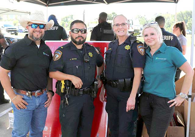 Two sheriff's deputies and two North Houston DIstrict staff members pose together under a tent at National Night Out 2024. The scene features a vibrant outdoor setting.