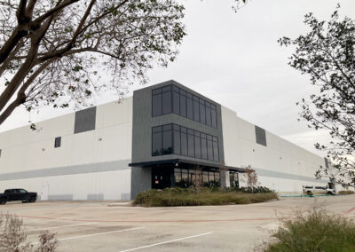 Large modern industrial warehouse with clean exterior panels, corner glass offices, and landscaped frontage.
