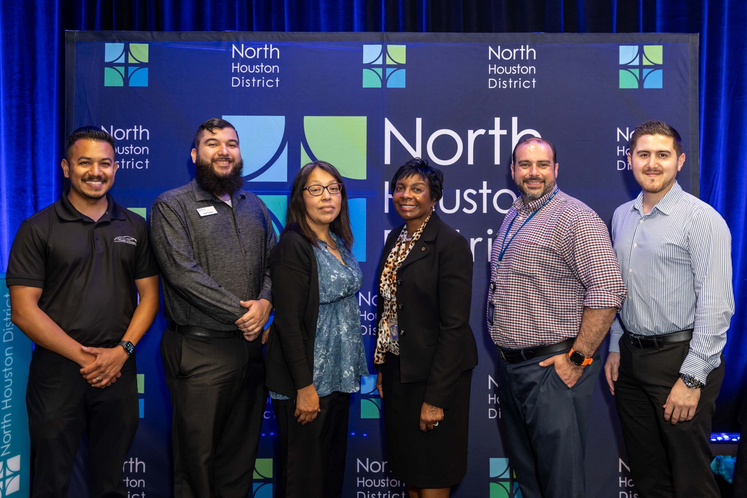 A group of six people from Frost Bank pose together in business attire in front of the North Houston District step-and-repeat.