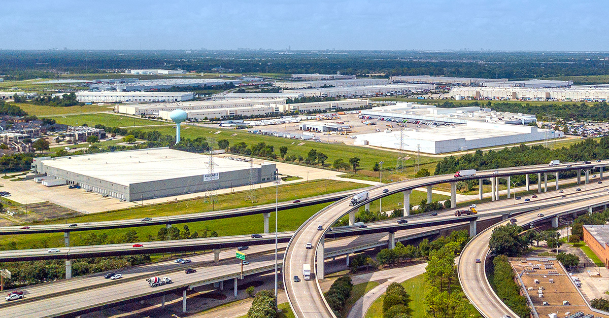 An aerial view of a highway interchange with multiple overpasses and surrounding industrial warehouses, highlighting transportation infrastructure serving a large logistics and distribution area.