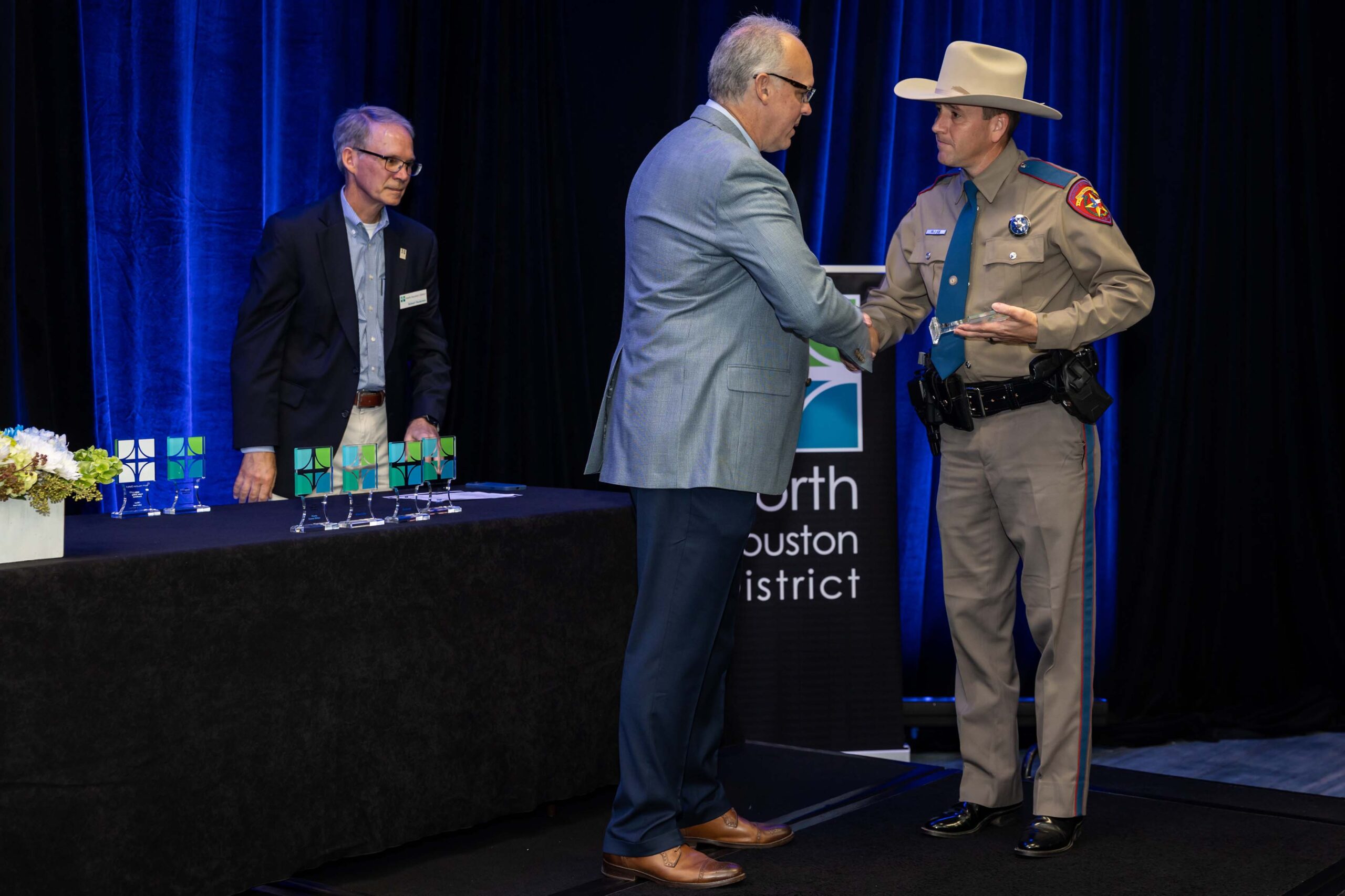 A Texas DPS Trooper receives an award plaque while shaking hands with a presenter on stage.