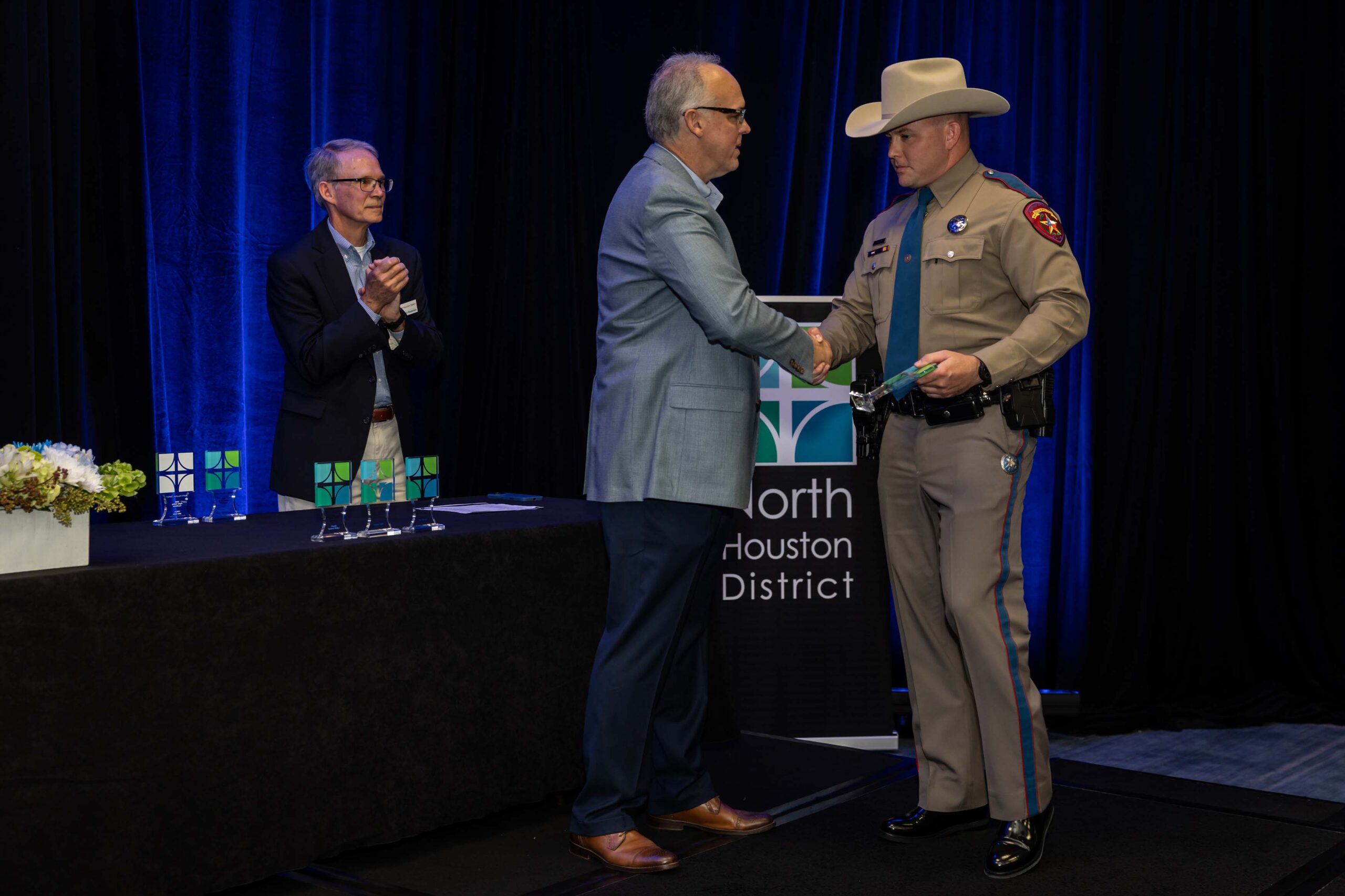 A different Texas DPS Trooper shakes hands with a presenter while holding his award plaque.
