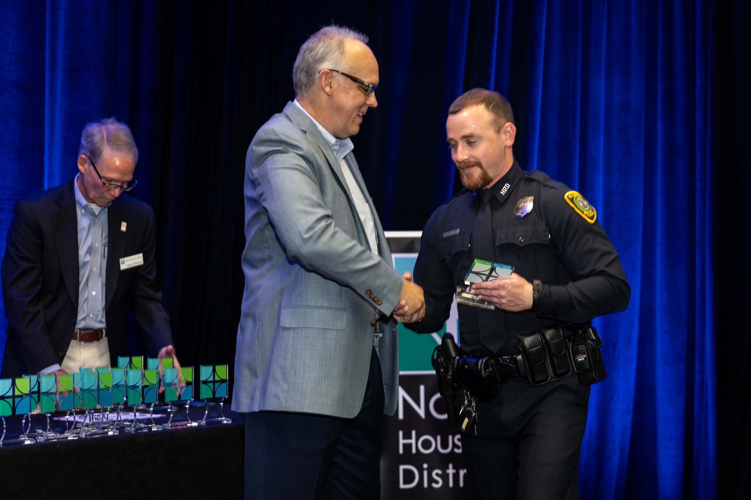 A uniformed officer accepts an award and shakes hands with a presenter during the 2025 North Houston District Public Safety Awards Luncheon.