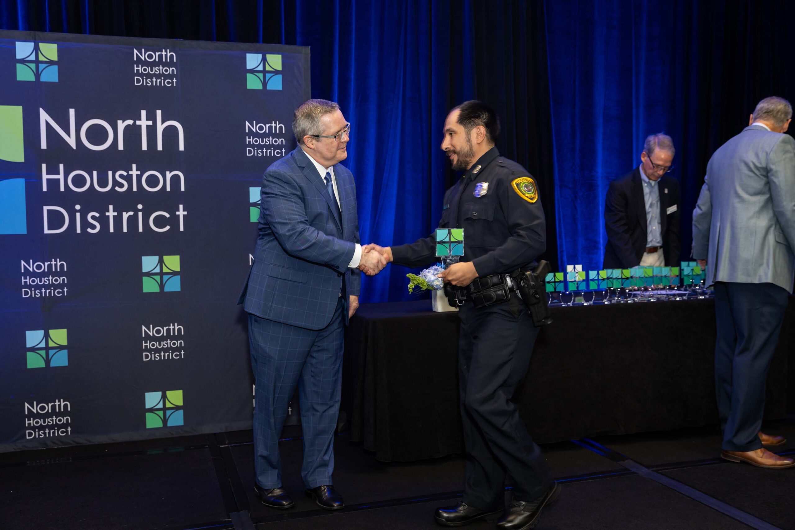 A uniformed officer accepts an award and shakes hands with a presenter during the 2025 North Houston District Public Safety Awards Luncheon.