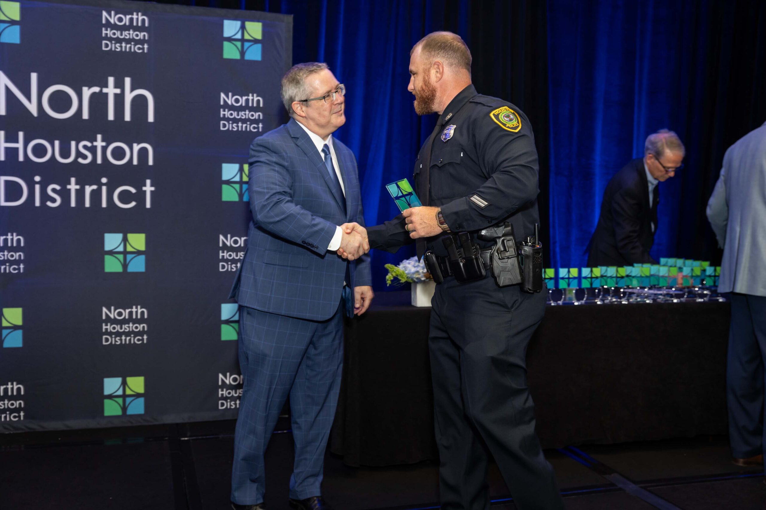 A uniformed officer accepts an award and shakes hands with a presenter during the 2025 North Houston District Public Safety Awards Luncheon.