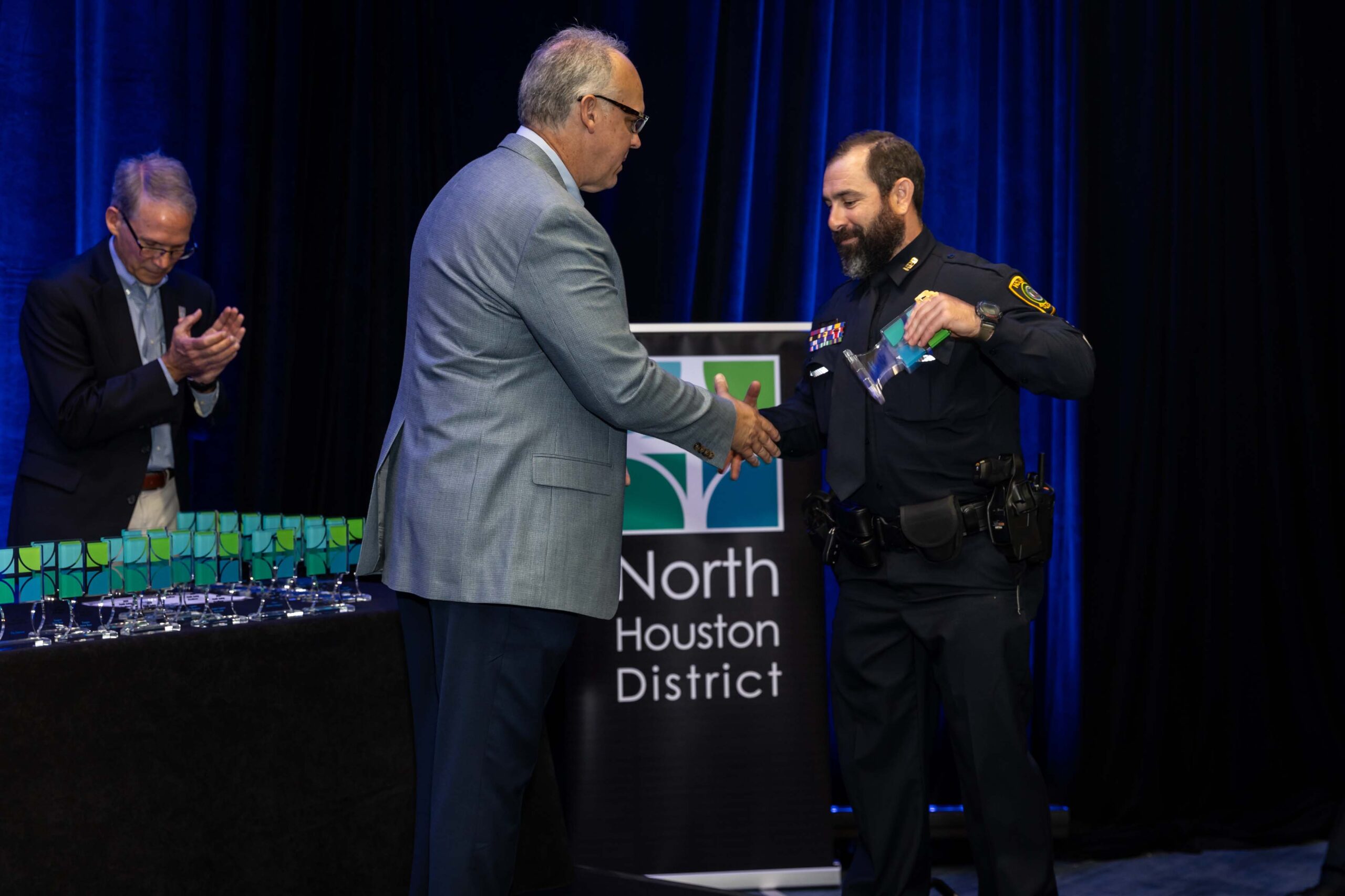 A uniformed officer accepts an award and shakes hands with a presenter during the 2025 North Houston District Public Safety Awards Luncheon.