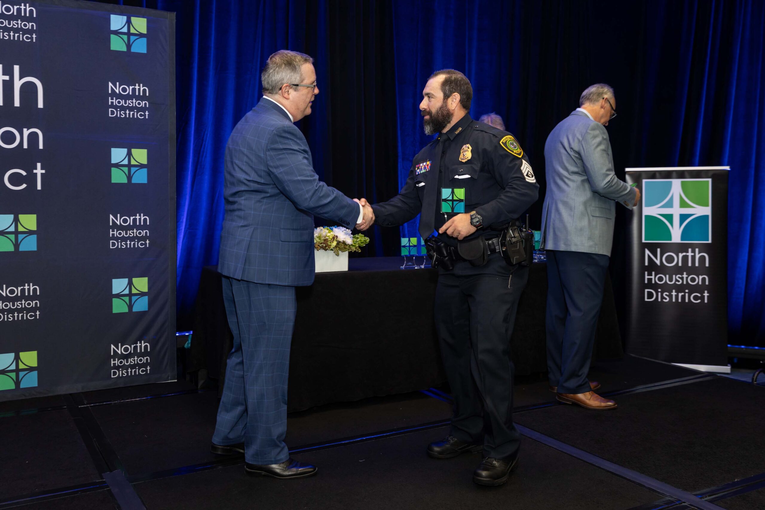 A uniformed officer accepts an award and shakes hands with a presenter during the 2025 North Houston District Public Safety Awards Luncheon.
