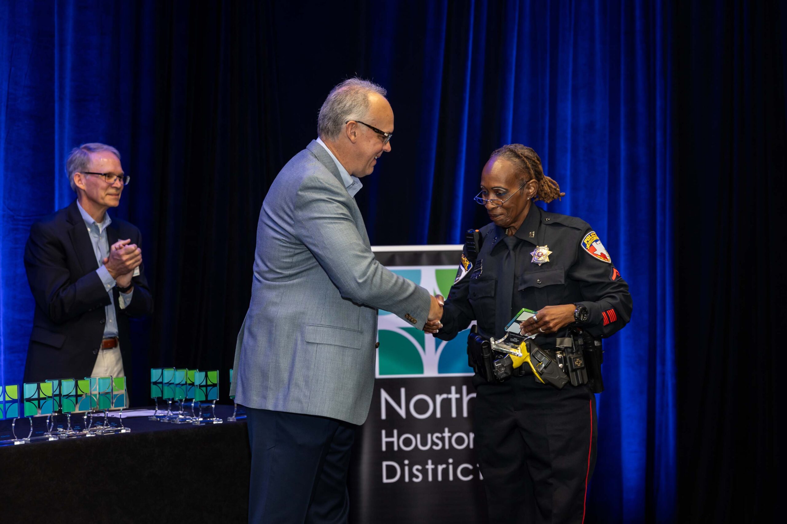 A uniformed officer shakes hands with a presenter on stage while receiving The Beacon Award at the 2025 Public Safety Awards.